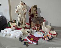 Wide shot of entire lot showing two large Santa figurines, assorted smaller Santa elf figures, pots, cotton snow decoration, wreaths, and various Santa-themed decor pieces arranged on a table.
