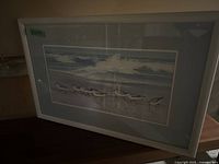 Framed seagull print leaning against a wall on a wooden surface.