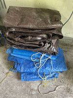 Stack of folded brown and blue tarps showing multiple layers and some securing rope