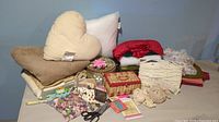 Overview of sewing lot including fabric, pillow inserts, sewing baskets, lace, buttons, pin cushions, and small sewing tools on a table.