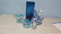 Photo showing all glass pieces including the tall smoky blue vase, tea light holders, crackle glass candle holder, smaller crackled vase, and frosted glass cat figurine.