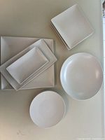 Overview of all stoneware items laid out showing round and square plates, serving bowl, and platters.