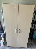 Front view of light wood-colored pressboard cupboard with two doors and silver handles.