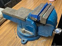 Angled side view of the blue table top vice showing the swivel base, handle, and steel jaws.