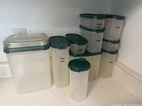 Photo showing multiple Tupperware Modular Mates containers with green lids, arranged on a counter. Some containers labeled with contents including brown sugar, walnuts, chocolate chips, coconut, and raisins.