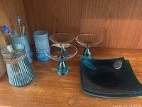 Turquoise glassware including ribbed vase with rope, frosted cylindrical vase, square plates, footed bowls, and cocktail picks