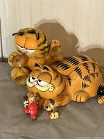 Photo showing plush Garfield window ornament with suction cups and vintage Garfield phone with small resin figurines surrounding them.