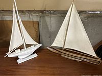 Two vintage sailboat models side by side on a wooden surface in front of a plain background, showing overall condition and relative size.