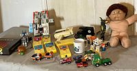 Lot overview showing various vintage toys including Fisher Price movie viewer, Cabbage Patch doll, transformers figure, Matchbox cars, Sesame Street toys, and Raggedy Ann/Andy resin dolls.