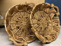 Top view of two large round low wicker baskets with woven flat and round strips and looped edge design, placed side by side on a flat surface.