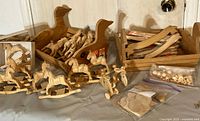 Photo showing two wooden crates shaped like ducks, multiple small wooden rocking horses, and some small round wooden beads on a tabletop.