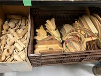 Box containing various unfinished wooden crafting pieces including turned candlesticks, spindles, and handles.