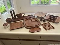 Overview of wooden kitchen serving pieces placed on counter, including bowls, trays, salt and pepper grinders, and ceramic container.