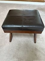 Front view of wooden foot stool with black upholstered seat showing overall structure