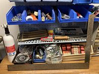 Photo showing blue plastic bins holding door hardware (knobs, handles), various tools including a large glass and tile cutter with wooden handle, Exacto knives, and a Master Lock padlock with key.