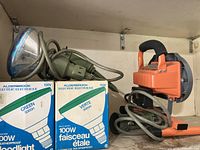 Two HDX flood work lights with attached cords and two unopened boxes of Aldersbrook 100W 130V floodlight bulbs.