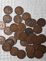 Array of Canadian pennies from 1937 and 1938 spread on white cloth showing obverse and reverse sides