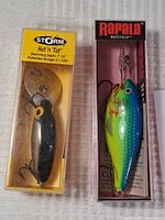 Photo of Storm Hot 'n Tot fishing lure in original yellow plastic packaging showing front and side of lure with treble hooks visible.
