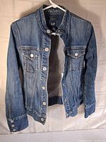 Front view of the blue GAP denim jean jacket hanging on hanger showing button details and classic design.