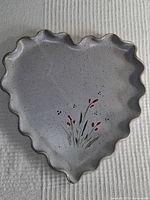 Photo of gray heart shaped ceramic plate with scalloped edges and red floral painting.