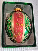 Front view of large oval-shaped Christmas tree ornament in original box showing detailed glitter design with green, pink, gold, and red colors.