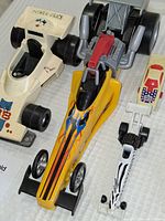 Top-down view of both Mattel and Fisher-Price dragster toy cars showing the Mattel yellow flame-detail Shakengo dragster and the white Fisher-Price dragster with number 88 decals.