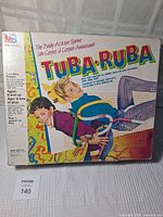 Front and side views of the MB Tuba-Ruba game box showing colorful graphics and children playing the game involving plastic tubes wrapped around their bodies.