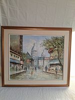 Framed acrylic painting showing overall Paris street scene with people and architecture.