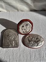 Three small silver covered plaques laid out on a white cloth background showing size and detail