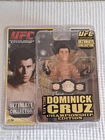 Front view of the new UFC Dominick Cruz figure in sealed blister packaging with clear display showing the figure holding a championship belt.