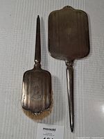 Full set of vintage metal hand mirror and brush displayed on a white cloth background.