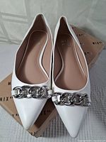 Front angled shot of the pair of white women's dress shoes with silver chain detail on top of branded MixNo6 box.