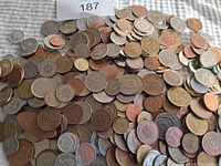 Photo showing a large assortment of used world coins spread on a fabric surface. Various coins with different sizes, metals, and designs are visible.