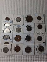 Overview photo of 17 assorted world coins in individual holders with labels including country and dates, placed on a fabric surface.