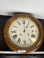 Front view of round oak clock with Roman numeral dial and brass bezel.