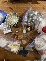 Top view of assortment of baking items on wooden surface including brioche moulds, cookie cutters, cookie press parts, and muffin liners.