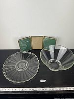 View of clear glass salad bowl and patterned serving plate with measuring tape beneath showing size