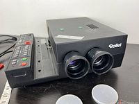 Black Rollei slide projector showing dual lenses and part of control panel and power cord.