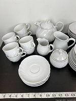 Full set overview showing cups, saucers, plates, teapot, creamers, sugar bowl in white glossy swirl embossed porcelain.
