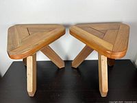 Two small vintage wooden stools with triangular tops and three angled legs each, placed side by side.