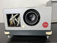 Front side of Leitz Wetzlar Leica Pradovit slide projector showing lens, power cord storage, and Leitz logo.