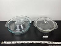 Two clear glass Pyrex baking dishes with lids placed on a dark surface, ruler included for size reference.