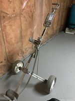 Full view of the metal 2-wheeled golf cart with the score card holder on top of the handle and straps for holding a golf bag.