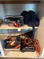 Shelf with air compressor box, blue coveralls, Motomaster battery charger and its box