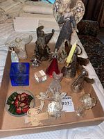Photo showing a variety of angel figurines made from brass, glass, wood, and ceramic including a large ceramic angel decorated with floral motifs, glass angels, brass angels, and decorative items like a red glass sun catcher and blue glass cube.