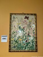 Framed botanical artwork with flowers and butterflies hanging on wall with orange background.