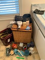 Photo showing a collection of bathroom items grouped around a wicker hamper including hair dryer, toothpaste tubes, soap bars, hangers, and small toiletry bags.