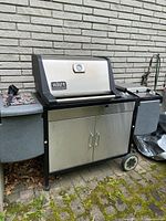 Full view of grill showing stainless steel lid, side shelves, lower cabinet and wheels
