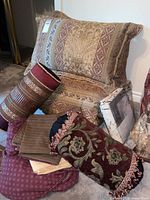 Gold base floral comforter with matching large pillows, round pillows, unopened twin duvet cover, burgundy sheet set and pillowcases arranged on carpeted floor