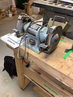 Side view of Delta bench grinder showing whole unit on wooden bench with manual beside it.